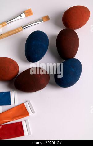 Fotofarbene dekorative Eier auf weißem Hintergrund mit Farben und Pinseln Stockfoto