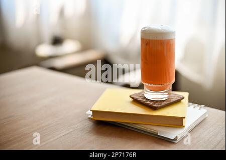 Ein Glas Thai-Eistee steht auf einem Buch auf einem Holztisch im minimalistischen Café. Getränkekonzept Stockfoto