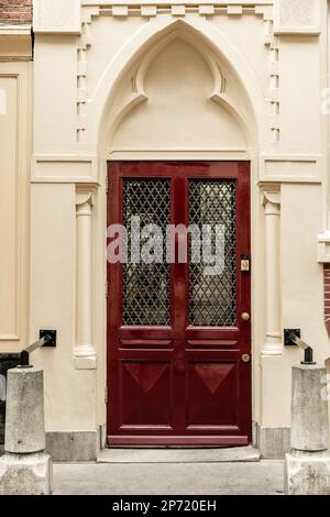 Amsterdam, Niederlande - 10. April 2021: Eine rote Tür an der Seite eines weiß bemalten Gebäudes vor einem Bogenfenster Stockfoto