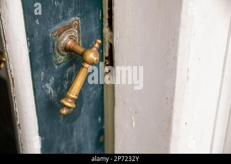 Ein alter Türgriff an einer weißen Holztür mit blauer Farbe und rostigen Metallknöpfen in der Mitte Stockfoto