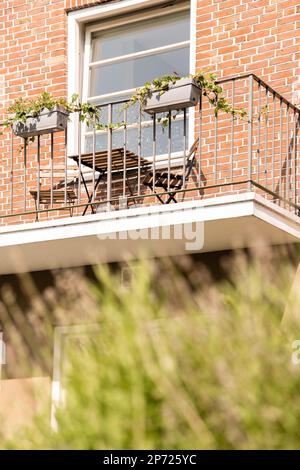 Amsterdam, Niederlande - 10. April 2021: Ein Balkon mit Pflanzen, die auf dem Balknotn-Geländer wachsen, und ein offenes Fenster auf dem Foto sind verschwommen Stockfoto