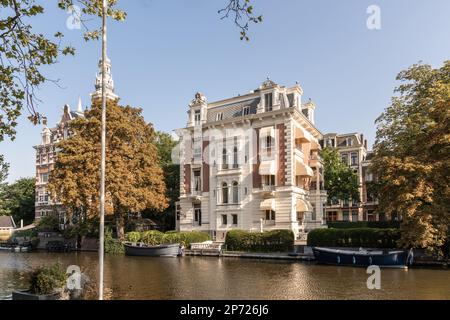 Ein altes Gebäude an der Seite eines Flusses mit Booten vor dem Hotel und Bäumen am Ufer dahinter Stockfoto