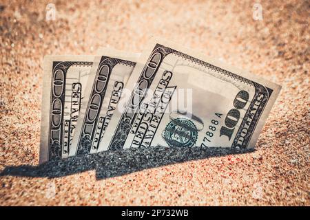 Gelddolare, die halb mit Sand bedeckt sind, liegen in der Nähe des Strandes. Geld wächst aus dem Boden. Dollarscheine teilweise im Sand am Meer verschüttet Strand Konzept Finanzierung Geld Urlaub entspannen Urlaub. Stockfoto