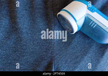 Moderner Rasierer auf grauem Tuch. Dieses Gerät zum Entfernen von Fusseln von Kleidung. Stockfoto