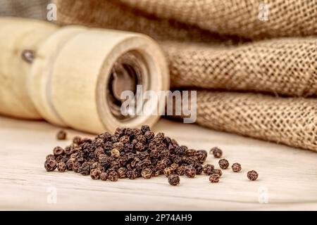 Holzpfeffermühle und schwarzer Pfefferkorn Stockfoto