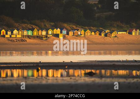 Reflexion von Strandhütten in Abersoch, die bei Sonnenaufgang leuchten Stockfoto