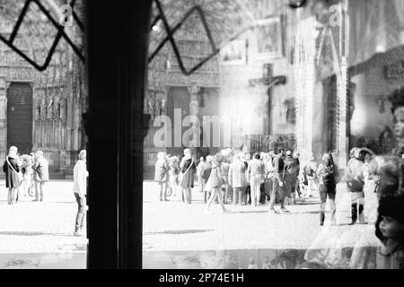 Straßburg, Frankreich - 20. März 2015: Schwarz-weiß abstrakte Kathedrale Notre Dame de Strasbourg Haupteingangsfassade mit Silhouetten von Menschen, Fußgängern, Einheimischen und Touristen, die sich im nahegelegenen Fenster mit einem Souvenirladen widerspiegeln Stockfoto