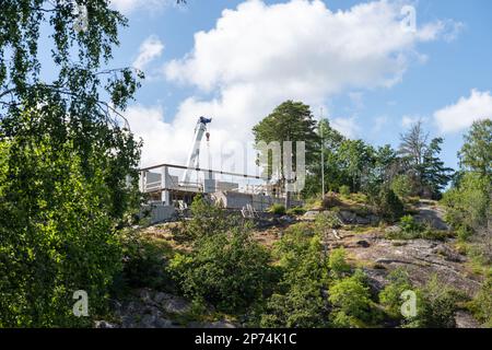 Weißer Mobilkran, der über ein Haus auf einem im Bau befindlichen Hügel ragt Stockfoto