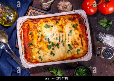 Hausgemachte Cannelloni-Pasta, großes Tablett mit gebackenen Cannelloni mit Hackfleisch mit Béchamel-Sauce, mit Kräutern in Zutaten auf dunklem Hintergrund Stockfoto