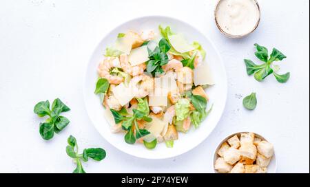 Caesar Salat mit Garnelen, Eisberg und Lammsalat, Croutons, Parmesan mit caesar Dressing. Weißer Tischhintergrund, Draufsicht Stockfoto