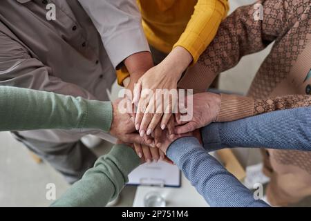 Draufsicht von Senioren, die während einer Selbsthilfegruppensitzung im Altersheim Hände im Kreis stapeln Stockfoto