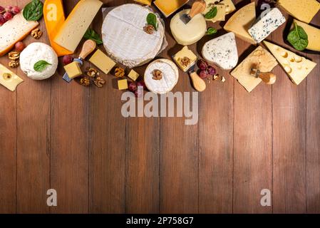 Verschiedene Käsesorten. Käseplatte mit verschiedenen Käse, mit Trauben, Nüssen, Käsemesser und Gewürzen, Holzhintergrund Kopierraum Stockfoto