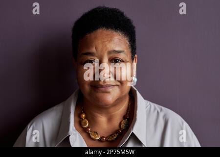 Vorderansicht von einer älteren schwarzen Frau, die vor violettem Hintergrund vor der Kamera lächelt Stockfoto