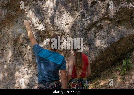 Männlicher Kletterlehrer zeigt den richtigen Weg zum erfolgreichen Klettern für weibliche Kletteranfänger Stockfoto