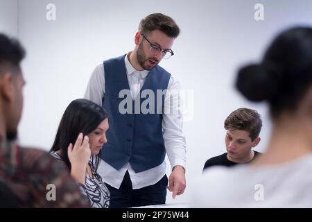 Lehrerin, die verschiedene ethnische Gruppen von weiblichen und männlichen Schülern im College-Raum unterrichtet; Stockfoto