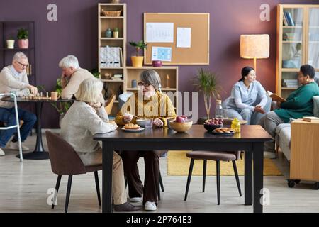Voller Blick im Gemeinschaftsraum im Seniorenheim mit vielfältigen Seniorengruppen, die Freizeitaktivitäten genießen Stockfoto