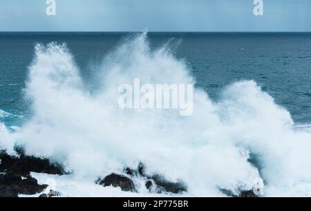 Wellen schlagen auf Felsen und bilden große Wassersäulen Stockfoto