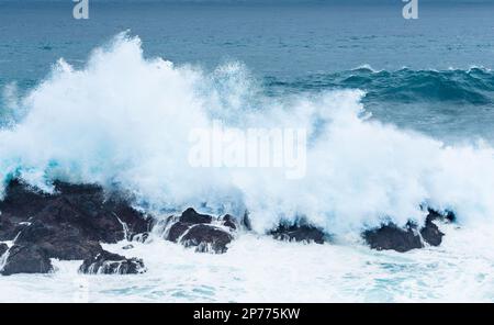 Wellen schlagen auf Felsen und bilden große Wassersäulen Stockfoto