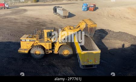 Radlader lädt Erde auf Lkw und arbeitet auf einem riesigen Bergbaugelände. Stockfoto