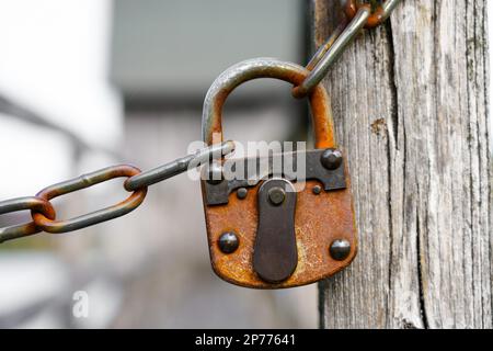 Altes rostiges Schloss, das an der Kette hängt. Altes Vorhängeschloss. Stabiles Schloss zum Zusammenhalten einer Kette vor einem Durchgang. Stockfoto