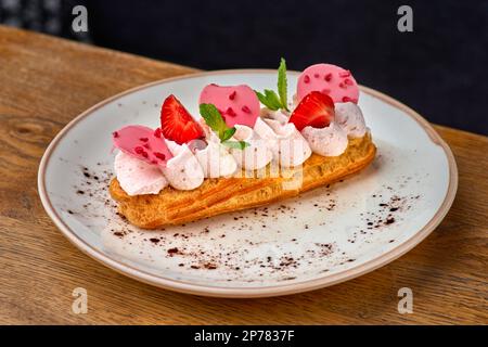 Eclairs mit Sahne und Erdbeeren auf einem weißen Teller. Stockfoto