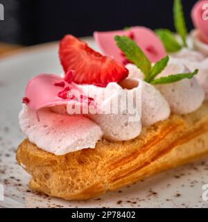 Eclairs mit Sahne und Erdbeeren auf einem weißen Teller. Nahaufnahme auf dem Tisch, serviert in einem Restaurant, Speisenkonzept. Stockfoto