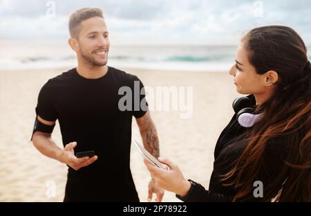 Junges Paar aus Mann und Frau, das Sportbekleidung trägt, Smartphones am Meer benutzt, sich auf das Training vorbereitet Stockfoto