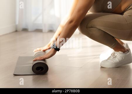 Unbekannte sportliche Frau, die Yoga-Matte rollt, zu Hause trainiert Stockfoto