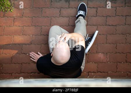 Top Aussicht auf einen jungen weißen Mann, der müde und besorgt auf dem Bürgersteig saß. Angstzustände, Depressionen Stockfoto