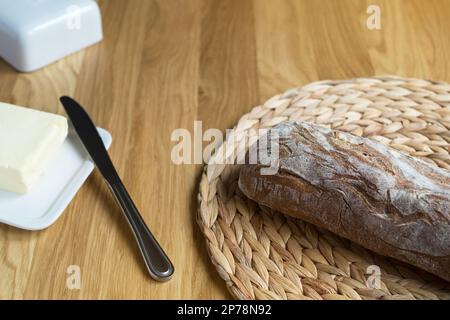 Knusprige Ciabatta auf einer kreisförmigen gewobenen Serviette aus Wasserhyazinthe, Butter auf weißem Buttergericht. Frisches Brot, gebratene Kruste. Italienisches Essen. Stockfoto
