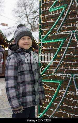 Der Junge stand auf einer Weihnachtsmesse neben einem künstlichen Weihnachtsbaum Stockfoto