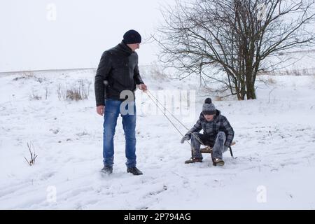 Der ältere Bruder zieht im Winter mit seinem jüngeren Bruder Schlitten auf Schnee Stockfoto