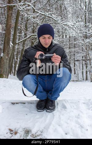 Im Winter setzt sich ein Mann auf eine Amateurkamera und fotografiert die Natur Stockfoto