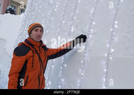 Ein Mann, der im Winter neben einem großen weihnachtsball auf dem Platz steht Stockfoto