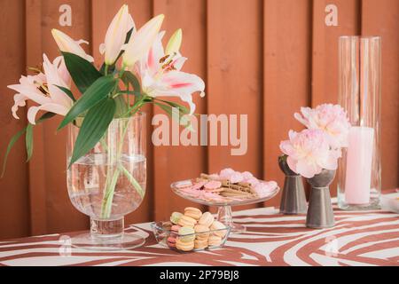 Lilienblüten in Glasvase und Makronen auf dem Tisch. Blumenstrauß in Vase auf Schokoriegel. Stockfoto
