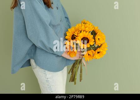 Frau mit einem Sommerstrauß Sonnenblumen auf grünem Wandhintergrund, Platz kopieren Stockfoto