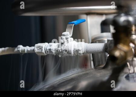 Flüssigstickstoff gefrorener Wasserhahn und Hebel. Sichtbarer schwimmender weißer Kondensationsrauch aus dem unter Druck stehenden Tank, isolierte Nahaufnahme. Stockfoto