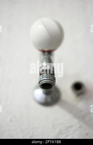 Altmodischer Wasserhahn aus Metall und weißem Ebonit, an der Wand montiert, in der öffentlichen Waschküche Nahaufnahme, geringe schmale Tiefenschärfe. Stockfoto