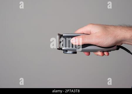 Elektrischer Haarschneider, der von einem männlichen Kaukasier in der Hand gehalten wird Nahaufnahme Vorderansicht isoliert auf Grau. Stockfoto