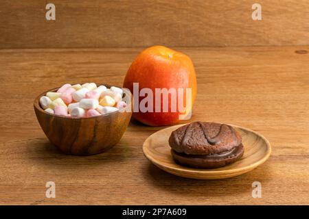 Kakao Marshmallow Schokoladenkuchen auf Holzteller mit Marshmallow in Holzschüssel und rotem, reifem Apfel auf Holztisch Stockfoto