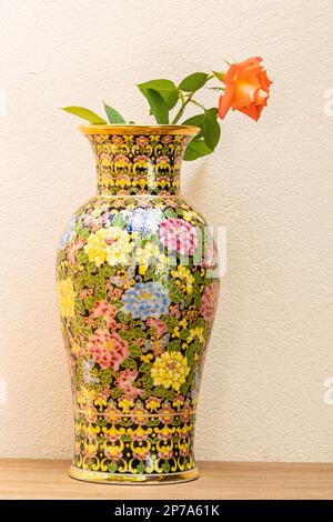 Benjarong-Vase mit roter Rose auf Holztisch. Wunderschönes Souvenirprodukt aus Thailand, Benjarong Vase. Benjarong ist in fünf Jahren thailändisches Porzellandesign Stockfoto