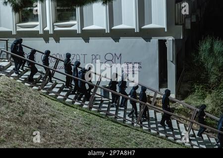 Barcelona, Spanien. 08. März 2023. Mit Kapuzen versehene Schüler marschieren nach unten mit Schriftzeichen an der Wand im Hintergrund, die sich auf den 8M (den internationalen Frauentag) während des Streiks zum Frauentag beziehen. Die Studenten der Autonomen Universität Barcelona veranstalteten am 8. März anlässlich des Internationalen Frauentags einen Streik und blockierten den Zugang zur Autonomen Universität von Barcelona für Studenten, die den Unterricht besuchen, um eine viel feministischere Perspektive im Bildungssystem zu fordern. Kredit: SOPA Images Limited/Alamy Live News Stockfoto