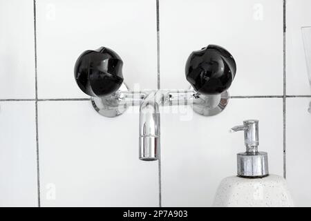 Waschbecken und Wasserhahn im Badezimmer mit schwarzen Rührknöpfen und Spender für Flüssigseife. Nahaufnahme, keine Leute. Stockfoto