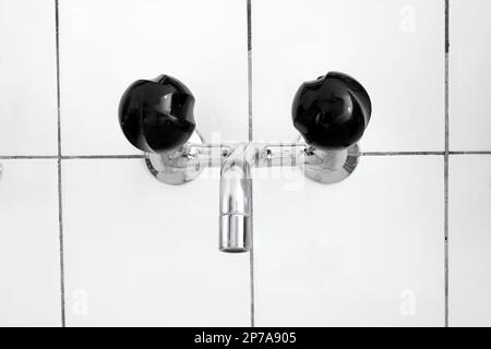 Waschbecken und Wasserhahn im Badezimmer mit schwarzen Rührknöpfen. Nahaufnahme, keine Leute. Stockfoto