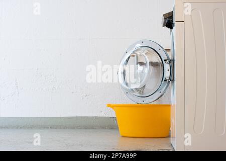 Waschmaschine im Landry Room, offene Tür und gelber Kunststoffkorb. Seitenblick, keine Leute. Stockfoto