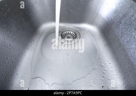 Fließender Strom von Leitungswasser in ein Metallwaschbecken. Lange Belichtung, keine Menschen, Weitwinkel. Stockfoto