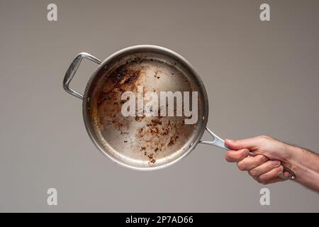 Dreckige, ölig verbrannte Bratpfanne aus Metall, die von Männern in der Hand gehalten wird. . Stockfoto