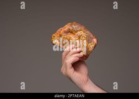 Rohes Gestell gewürzter Schweinerippchen in männlicher Hand, Nahaufnahme, isoliert auf braunem Hintergrund. Studioaufnahme. Stockfoto