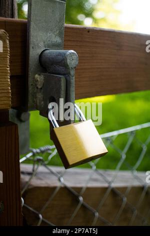 Massives Metallschloss an einem Zauntor mit Kettengliedern. Nahaufnahme im Freien, Sommer, Tag, Sonnenlicht, keine Menschen... Stockfoto