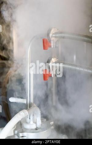 Flüssiges Stickstoffgas, das aus einem unter Druck stehenden Tank austritt und mit Metallrohren und roten Handventilen verbunden ist. Stockfoto